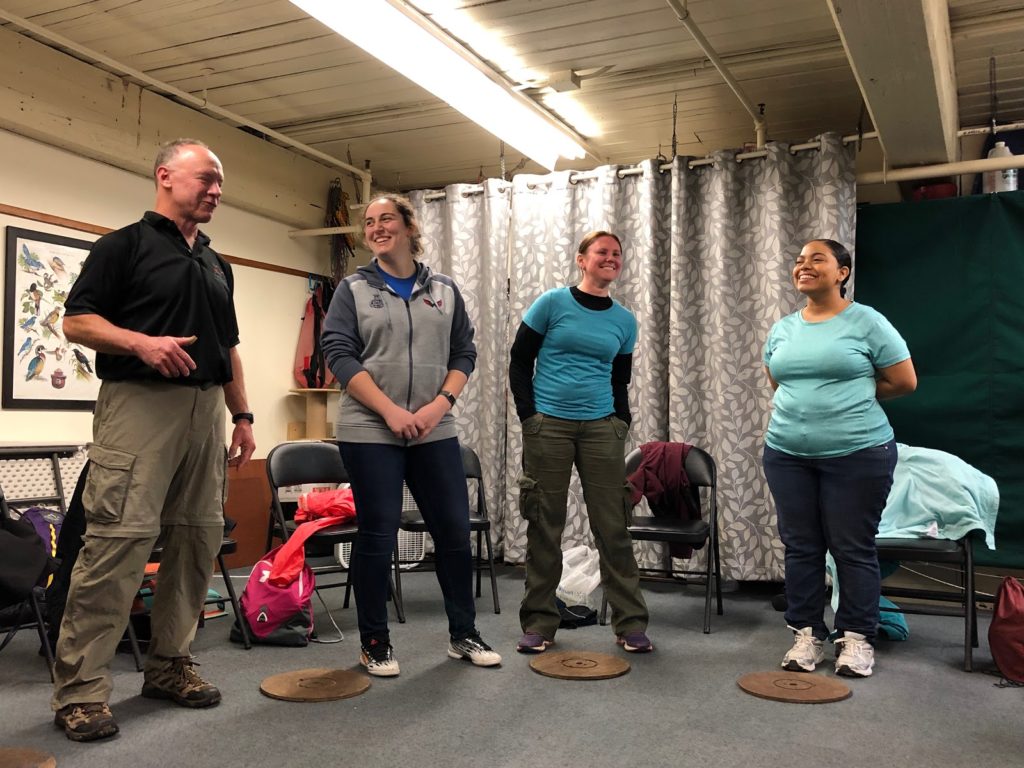 Three women and one man standing in a semi-circle and participating in a team building exercise.