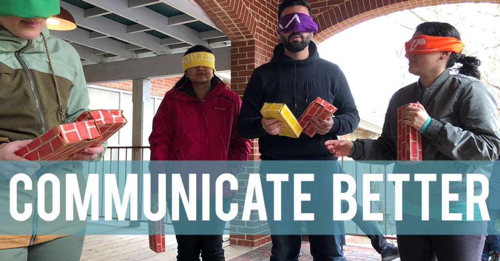 Blindfolded people holding colorful plastic bricks and awaiting instructions. The words Communicate Better are superimposed on the image.