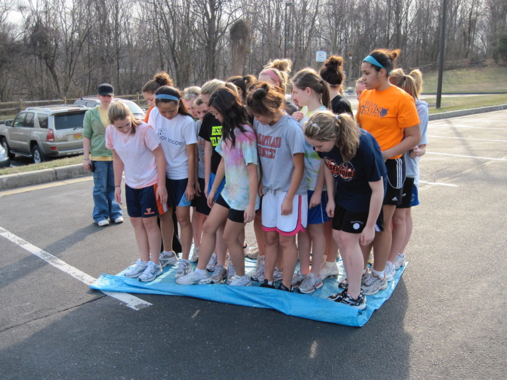 A group of teenagers try to stand together on a small carpet.