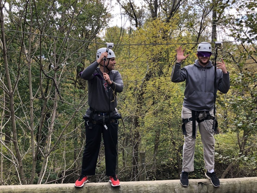 A man leading a blindfolded man on a high ropes challenge course.