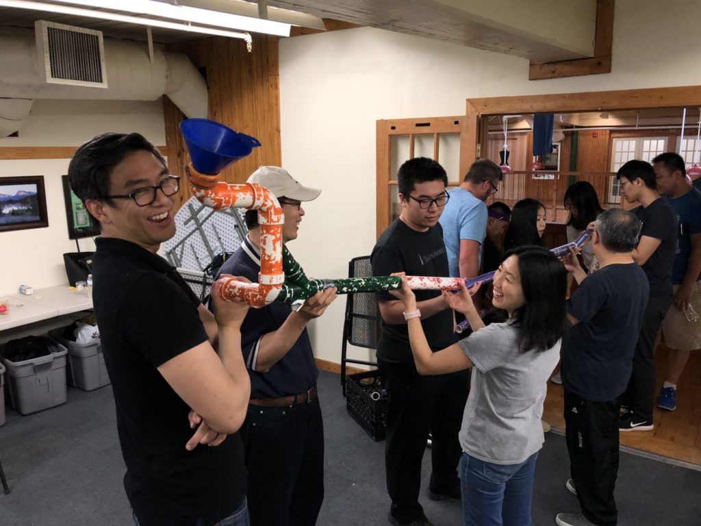 A group of people building up pieces of piping to create one continuous pipe.