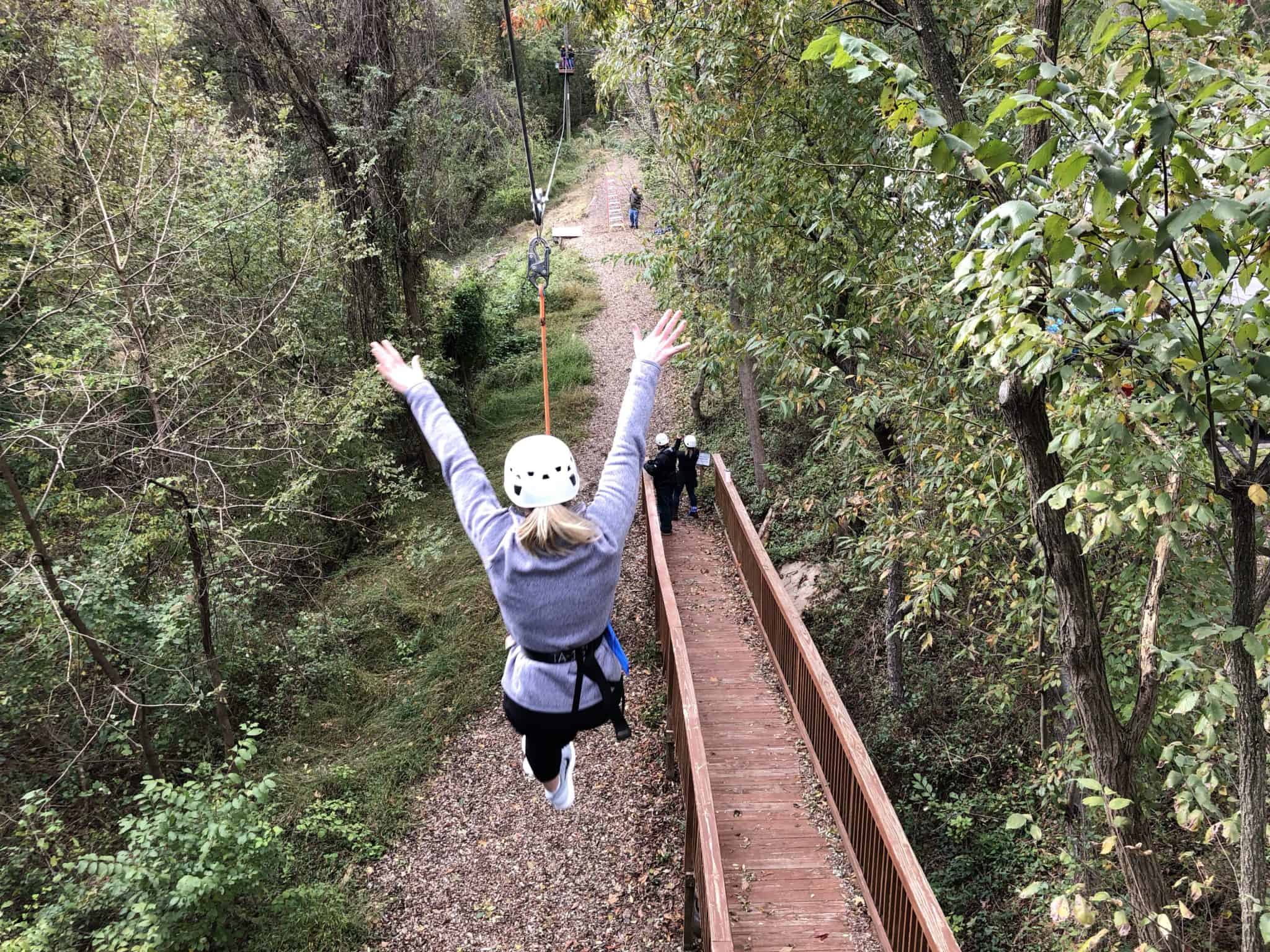 woman riding zip line with her arms raised.