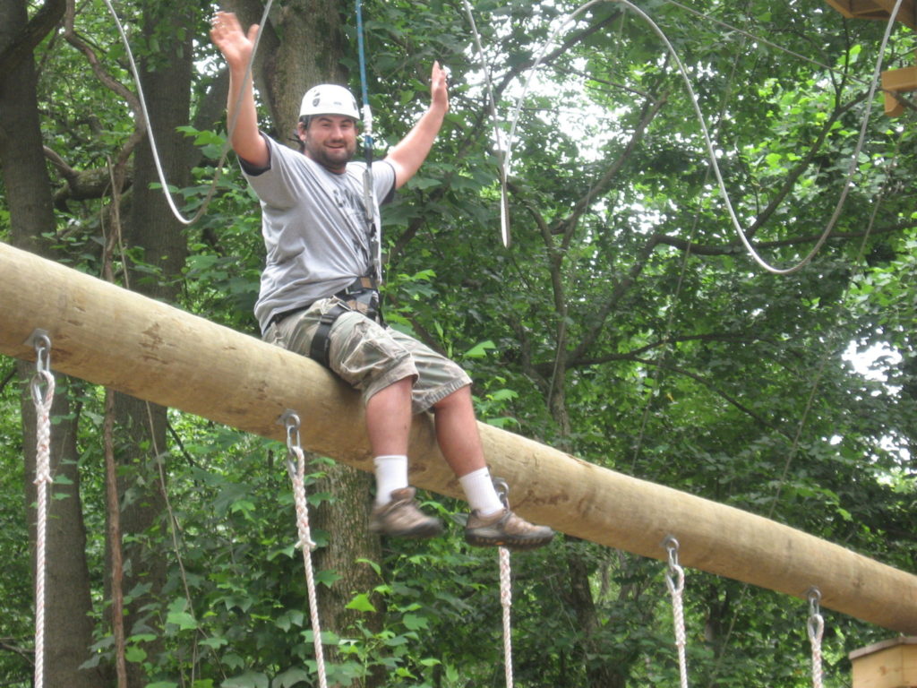 Man sitting on a log high in the air on a ropes course.