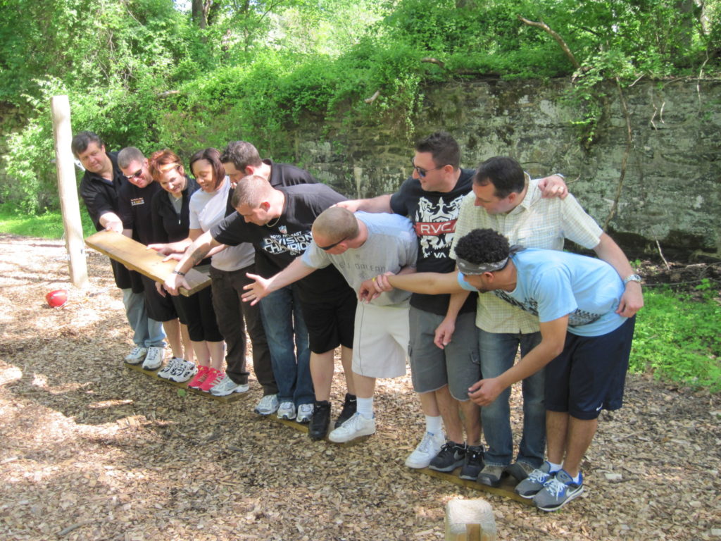 A group stands in a line and passes a 2x4 board down the line.